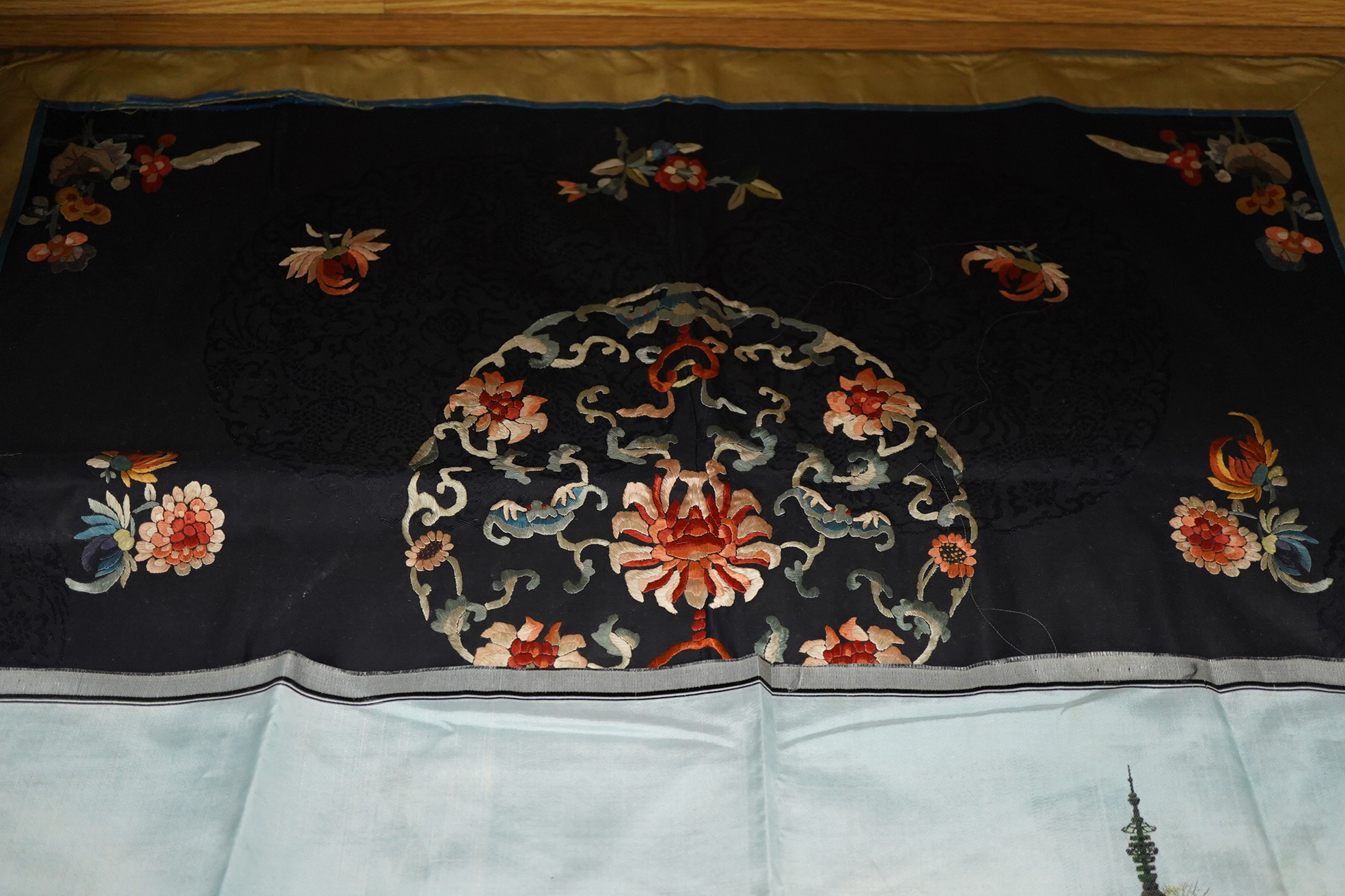 An early 20th century Chinese blue silk and coloured floral embroidered table cover, with a later Chinese printed panel of a house, pagoda and monument along a river bank, embroidery 78cm x 62cm. Condition - the edging t